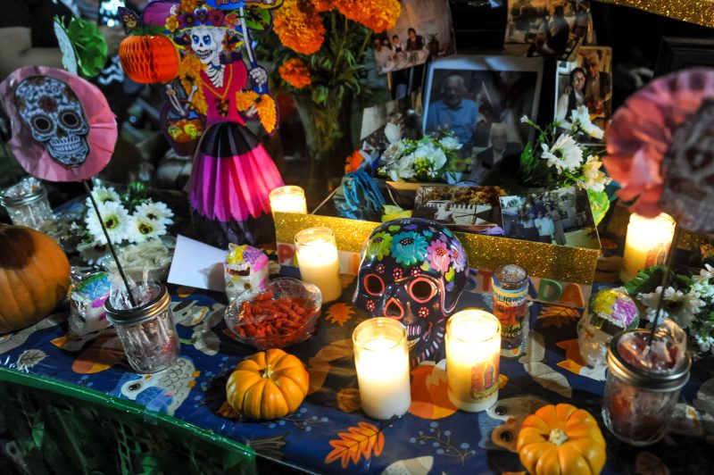 A decorative ofrenda has candles, skulls, photos and flowers