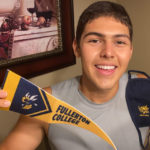A happy 2020 freshman holds up a Fullerton College pennant and mask