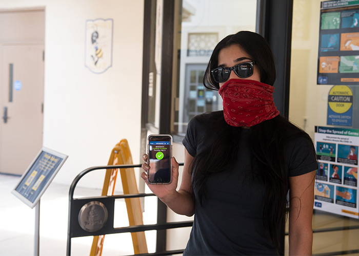 A students holds up her phone to show she has cleared the mobile self-screening survey and may attend class.