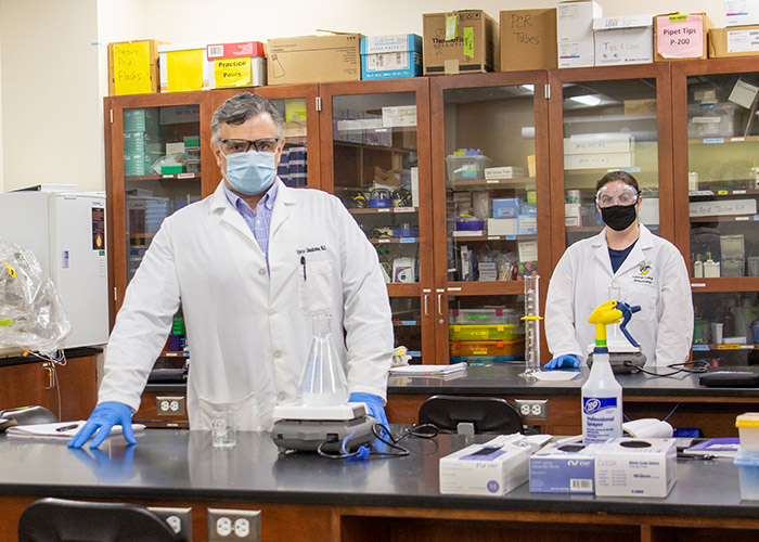 A faculty member and student wear masks and gloves in a lab classroom .