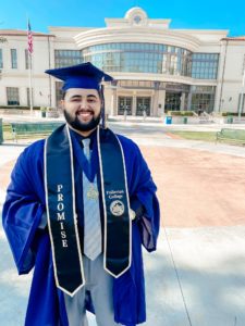 A student stands proud and smiling in his commencement regalia