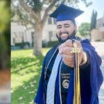A student stands proud and smiling in his commencement regalia