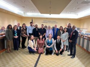 Several faculty are in a group and smiling at a board meeting where there were recognized for achieving tenure
